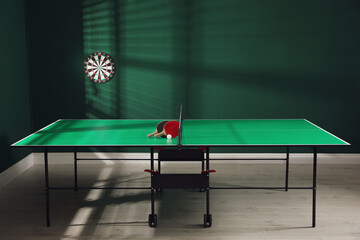 Green ping pong table with rackets and ball indoors