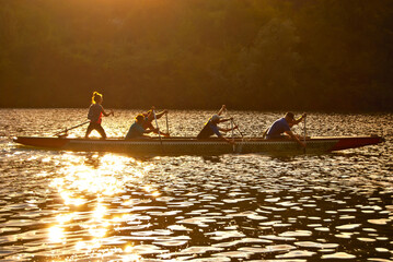 Canoeing. Dam training on the lake. Silhouettes of athletes on a sunset background. Sunny counter...