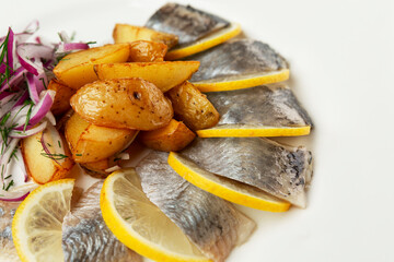 Sliced herring on a white plate with potatoes and red onions. Appetizing appetizer. Close-up.