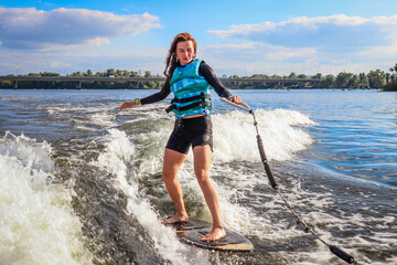 The girl is learning to ride a wakesurf on the river behind the boat. Wake vest. Board