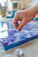 Female artist's hand sprinkling silver glitter on the fluid art picture
