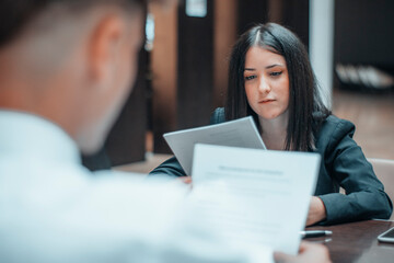 Mujer joven trabaja en equipo con su cliente con hojas de papel en una reunion sentada