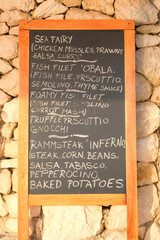 Chalkboard menu black color, message or advertising. Blackboard is standing near the restaurant in sea coast. Sunny day.