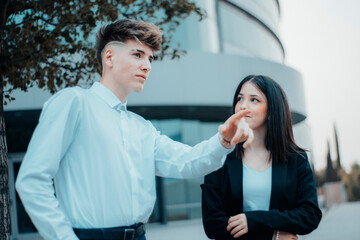 Chaval empresario señalando y mujer joven de pie con una sonrisa en su descanso de trabajo empresarial junto al edificio con cristaleras