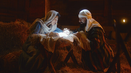 Mary and Joseph caressing baby Jesus in illuminated manger - obrazy, fototapety, plakaty