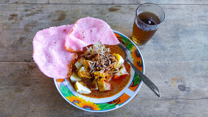 Photo of a traditional Indonesian food called kupat Tahu on a plate equipped with a spoon and a glass of fresh tea