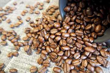 whole coffee beans spilling from a dark mug on a wooden table. side view