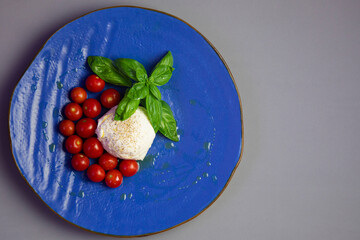 mozzarella , cherry tomatoes and basil on the blue plate on gray background