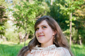 Portrait of a beautiful girl in a white dress looks thoughtfully and smiles in summer in nature