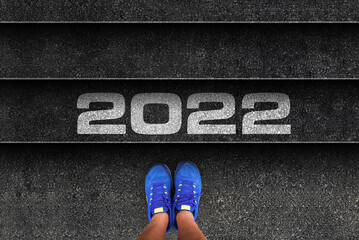 happy new year 2022. man legs in sneakers standing next to stairs with number 2022
