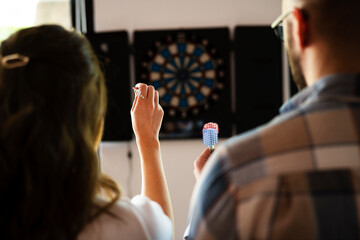 Young colleagues taking break after work. Happy young businessman and businesswoman playing darts...