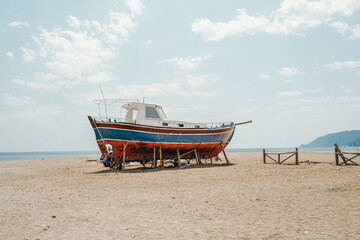 Fototapeta na wymiar Lonely abandoned old yacht on an empty sandy sea beach in summer