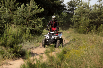 Man driving modern quad bike on sandy road near forest. Extreme sport