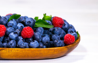 Blueberry and Raspberry With a Green Mint leaf in a Wooden Bowl on a white top view, Summer Freshly Berry, Copyspace