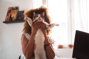 A young woman sits in the home office and plays with the cat while taking a break from work.