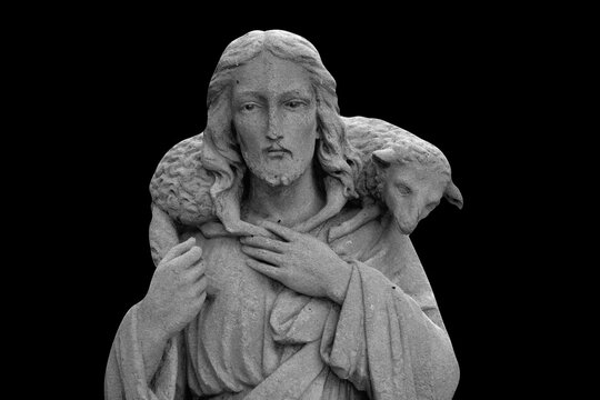 Ancient statue of Jesus Christ is the Good Shepherd with the lost sheep on his shoulders. Black and white image. Isolated on black background.