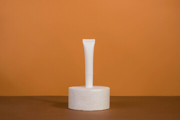 Unbranded bottles in mockup style. Tube of eye cream on a white podium on a beige background. Beauty background with facial cosmetic products. Spa, beauty concept.