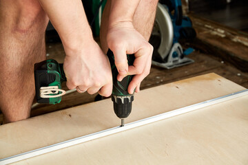 Electric power screwdriver. Carpenter working with hand tool on plywood. Close-up side view. Fixing the metal plank. Copy space. Labor day. Battery instrument. Operating rules and safety precautions