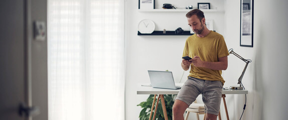 Man using smartphone at home while making pause from work.