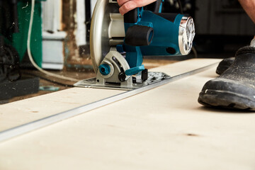 Fototapeta premium Sawing plywood by circular saw. Home repair. Hand tool. Man hold equipment. Building process. Woodworking. Safety engineering. Without gloves. Copy space. Indoor. Cutting material. Rental instrument