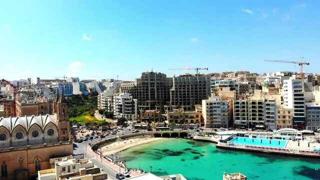 Aerial drone shot of St. Julians city, Balluta Bay Beach and The Parish Church of Our Lady of Mount Carmel in Malta island.
