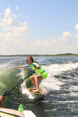 A girl is learning to ride a wakesurf on the lake behind a boat. Newcomer. Training. Wake vest