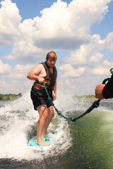 A man is learning to ride a wakesurf on the lake behind a boat. Newcomer. Training. Wake vest
