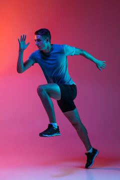 Portrat of Caucasian professional male athlete, runner training isolated on pink studio background with blue neon filter, light. Muscular, sportive man.