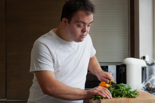 Young man with Down Syndrome cutting fresh vegetables in the kitchen