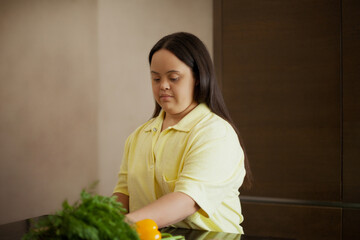 Young biracial woman with Down Syndrome cutting fresh vegetables in the kitchen