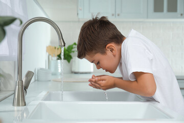 Boy drinking tap water over sink in kitchen