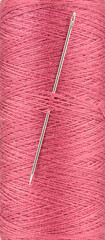 Full frame of red thread on spool and sewing needle in thread.