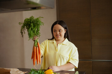 Young biracial woman with Down Syndrome holding fresh vegetables in the kitchen