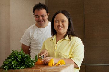 Young biracial couple with Down Syndrome cutting fresh vegetables and smiling