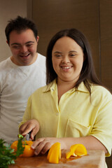 Young biracial couple with Down Syndrome cutting fresh vegetables and smiling