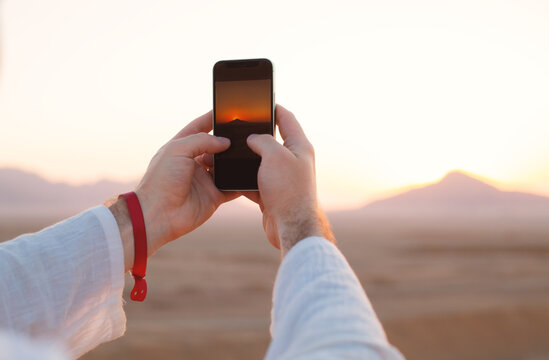 Male hands holding mobile phone with image of sunset or sunrise on the screen