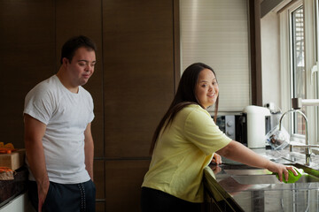 Young biracial couple with Down Syndrome cleaning the kitchen and smiling