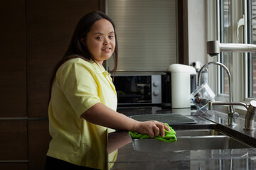 Young biracial woman with Down Syndrome cleaning the kitchen and smiling - Powered by Adobe