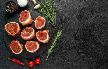 raw pork tenderloin medallions wrapped in bacon on a stone background  with copy space for your text	