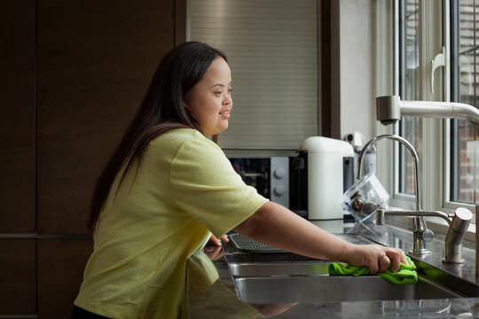 Young biracial woman with Down Syndrome cleaning the kitchen and smiling