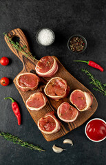 raw pork tenderloin medallions wrapped in bacon on a stone background