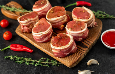 raw pork tenderloin medallions wrapped in bacon on a stone background