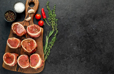 raw pork tenderloin medallions wrapped in bacon on a stone background 	with copy space for your text	