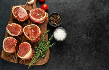 Fototapeta na wymiar raw pork tenderloin medallions wrapped in bacon on a stone background with copy space for your text 