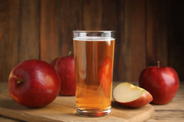 Glass of delicious cider and ripe red apples on wooden table