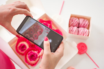 Woman is taking photo of homemade sweets, cupcakes and marshmallows using her smartphone. Food...