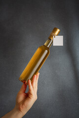 Male hand holding bottle of white wine, fruit alcohol liquor or natural oil with empty label on grey background. Mock up for brand, vertical shot