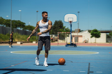 Chico joven atletico tatuado jugando a baloncesto en cancha azul