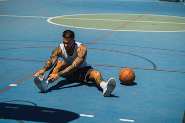 Chico joven atletico tatuado jugando a baloncesto en cancha azul