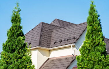 Tiled roof with segment of snow holding structure, Gutter system for metal roof. House with new brown metal tile roof and rain gutter. Metallic Guttering System, Guttering and Drainage Pipe Exterior